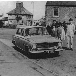 Photograph taken from Church Lane, looking across Sea Dyke Way towards the school house on the left.
The house in the centre of the photograph was demolished to make way for a road widening scheme which did not take place.
The people in the picture are :- L-R; Judy Maguire, Gordon Horry, Jill Smith. The lad on the right and the girl at the front are unknown.
The occupants of the early 1960s Vauxhall are also unknown.