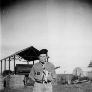 This photograph is of Stuart Grantham in his Boy Scout uniform and was taken around 1957/8.
However, in the background is the old pea vining shed housing the stationary pea viner. This was used in the days when a tractor and trailer would deliver the peas from the field to be "podded" in the stationary viner - before mobile pea viners were invented.
This was situated in Mill Lane and belonged to Mossops Farm.
The pea season was always an opportunity for the local children to wait in an advantageous place (i.e. under low hanging tree branches) waiting for pea to be knocked off the trailer and then eating them.
Sometimes they were grabbed directly from the back of the trailer - a rather more dangerous pursuit.