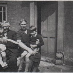 Charles Andrew Patrick and his wife Sarah Jane Patrick.
These were the parents of Margaret Burgess. They could be grandchildren they are holding.
The date of the photograph is uncertain but could be around the late 1940s/early 1950s
