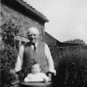Mr Tyler who brought up Kath Grantham seen here with Stuart Grantham in the high chair.
The photograph was taken in 1944 in the garden of the house the Granthams lived in which was situated in front of the Village Hall on Sea Dyke Way.  Now demolished.
To the right of the photograph can be seen the joiners shop - also demolished.